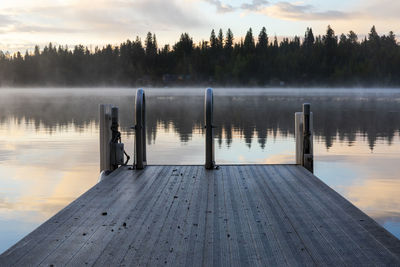 Swimming dock with ladder near calm lake at sunset with reflection