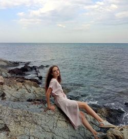 Young woman standing on rock by sea against sky