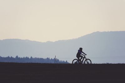 Woman riding bicycle on field against sky