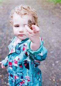 Cute baby girl holding pine cone standing outdoors