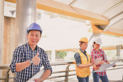 Portrait of male engineer showing thumbs up sign while standing by colleagues in bridge
