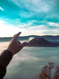 Cropped hand reaching mountains against sky