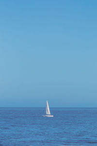 Sailboat in sea against clear blue sky