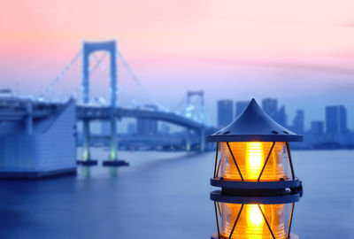 Illuminated suspension bridge over river during sunset