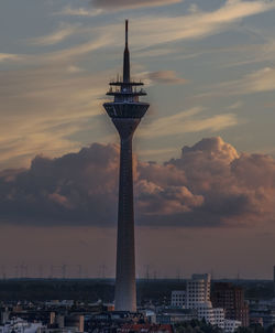 Communications tower in city against sky during sunset