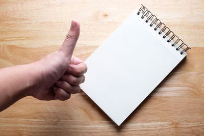 High angle view of person hand gesturing thumbs up over notepad on table