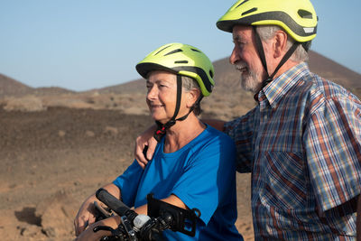 Smiling couple riding bicycles on field against clear sky