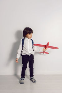 Boy child in a white shirt and jeans flies on a red airplane toy at the white wall of the house