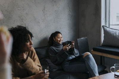 Smiling female entrepreneur using smart phone by colleague in break time at workplace