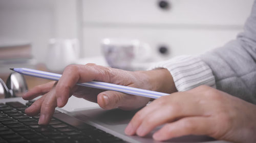 Cropped hands of businesswoman holding pen using mobile phone at office