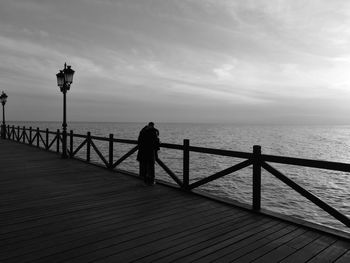 Man standing on railing by sea against sky