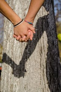 Low section of woman with hands on tree trunk