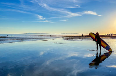 Low section of woman swimming in sea against sky during sunset