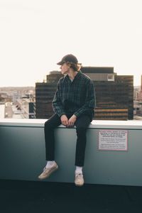 Young man looking away against built structure against clear sky