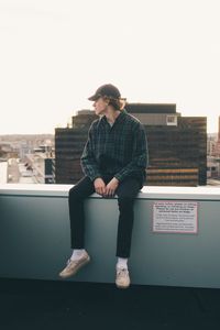 Teenage boy sitting on retaining wall against clear sky