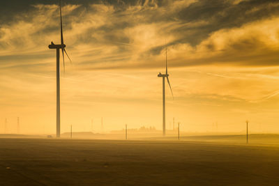 Wind turbines on field against sky during sunset