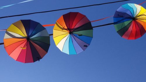 Low angle view of umbrellas against clear blue sky