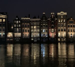 Illuminated buildings by river against sky at night