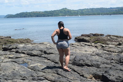 Rear view of young woman standing on rock by sea