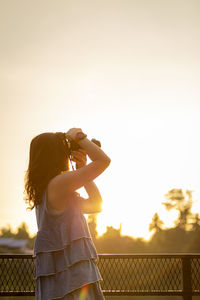 Woman photographing against sky during sunset