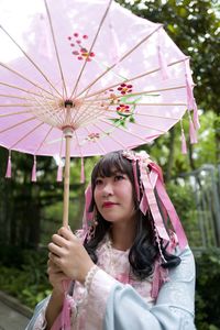 Portrait of woman with pink umbrella standing against plants