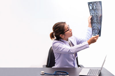 Female doctor examining x-ray image while sitting against white background