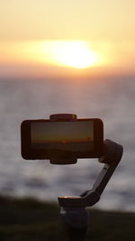 Close-up of camera on beach against sky during sunset