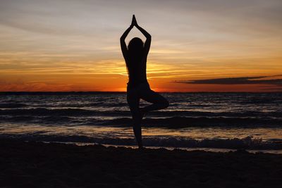 Silhouette man with arms raised on beach against sky during sunset