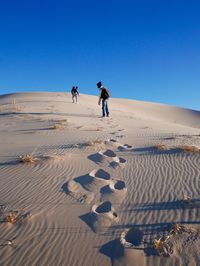 People on sandy desert against clear blue sky