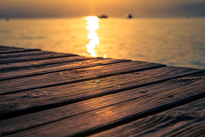 Sunlight on wood in sea against sky during sunset