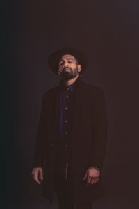Man wearing hat standing against black background