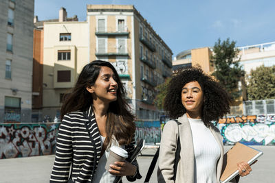 Female coworkers looking away while standing on street in city during sunny day