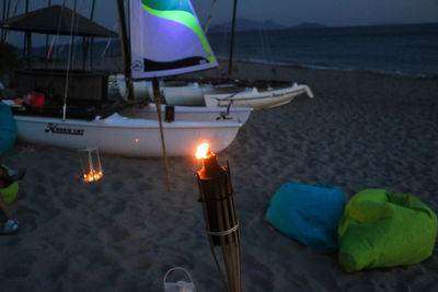 Close-up of illuminated candles on beach against sky