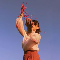 Low angle view of girl holding red against blue sky