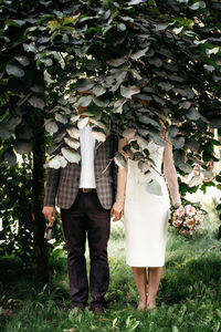 Rear view of friends standing by tree on field