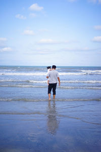 Rear view of man standing on beach against sky