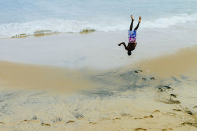 Upside down image of shirtless man in mid-air at beach