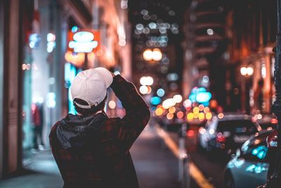 Rear view of man standing on illuminated street at night