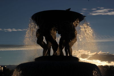 Silhouette man standing on rock at fountain against sky
