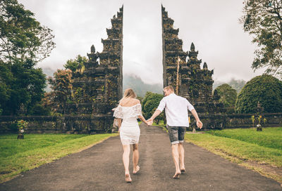 Couple walking on footpath at gate against sky