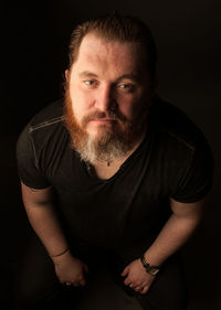 Portrait of man sitting against black background