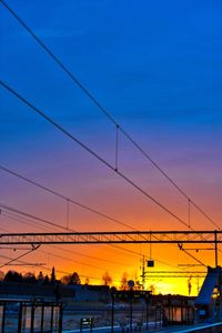 Power lines and buildings against sky during sunset