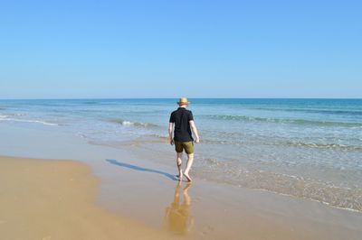 Rear view of man walking on beach against clear sky