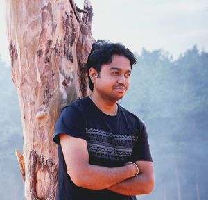 Portrait of young man looking away against tree trunk