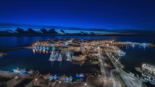 High angle view of illuminated city by sea against blue sky