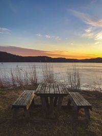 Empty bench by lake against sky during sunset