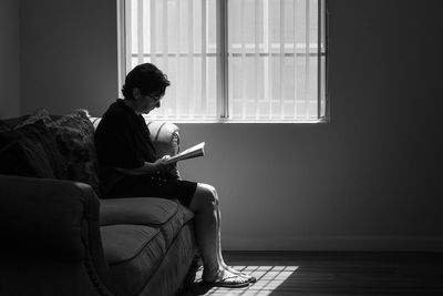 Silhouette mature woman reading book while sitting on sofa at home