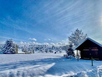 Snow covered field by building against sky