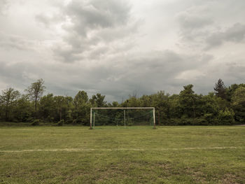 Trees on field against cloudy sky