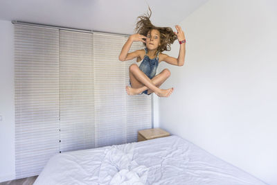 Portrait of girl jumping over bed at home